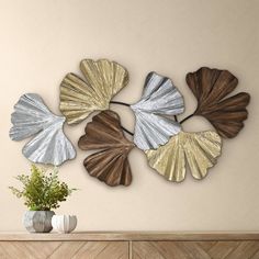 four metal leaf wall art pieces on a beige wall next to a vase and plant