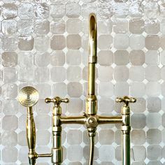 two brass faucets are on the wall in front of a mosaic tile background