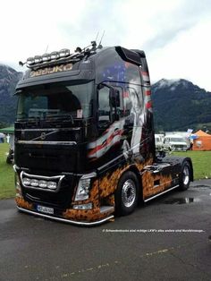 a large semi truck parked on top of a parking lot next to a mountain range