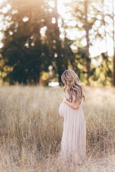 a pregnant woman standing in tall grass with her back to the camera