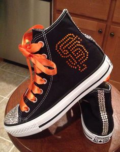 a pair of black sneakers with orange bows on the bottom and an orange shoelace