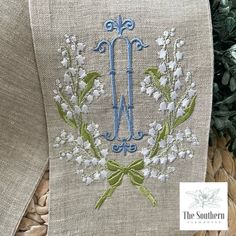 the embroidered monogrammed initial is on top of a tan cloth with white flowers and green leaves