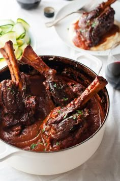 a pot filled with meat and sauce on top of a table next to a glass of wine