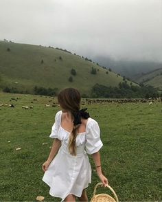 a woman walking across a lush green field holding a wicker basket in her hand