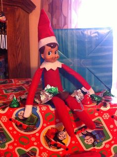 an elf sitting on top of a table with christmas wrapping around him and other toys