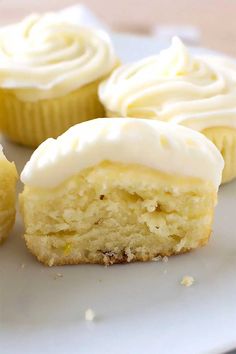 cupcakes with white frosting sitting on a plate next to each other and one cut in half