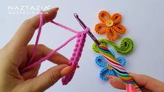 a person holding a crochet hook next to some colorful yarn and flower decorations