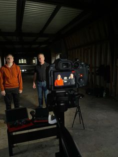 two men standing next to each other in a room with a camera on a tripod