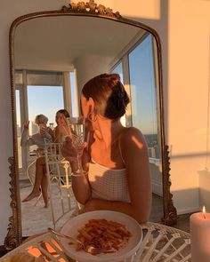 a woman sitting at a table in front of a mirror eating food from a bowl