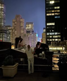 three people standing on top of a roof in front of the city skyline at night