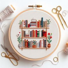 a cross stitch bookcase with books and flowers on it next to scissors, thread and spools