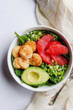 a white bowl filled with shrimp, avocado, and grapefruits