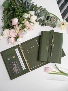 a notebook, pen and flowers on a table