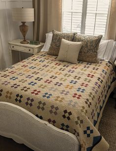 a bed with a quilt and pillows on top of it next to a night stand