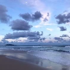 the sky is filled with clouds over the water at the ocean's edge as waves roll in