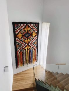 a rug hanging on the wall next to a stair case with glass railing and wooden handrails