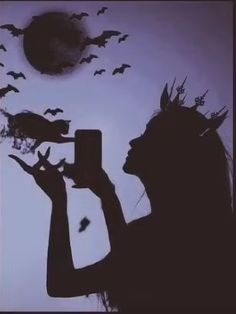 a woman holding up her cell phone in front of bats flying over her head and the sun behind her