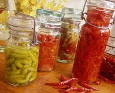 several jars filled with pickles and peppers on a wooden table next to other containers