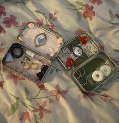 two small tins with various items in them on a flowered cloth covered bed