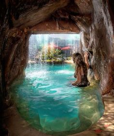 a woman sitting on the edge of a pool in front of a cave with water