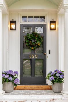 a front door with two potted plants and a wreath on the top of it