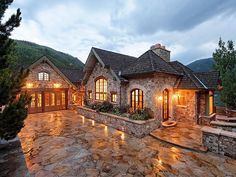 a stone house lit up at night with lights on the front porch and patio area