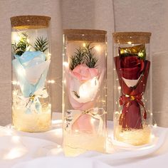 three vases with flowers in them sitting on a white tablecloth covered table cloth