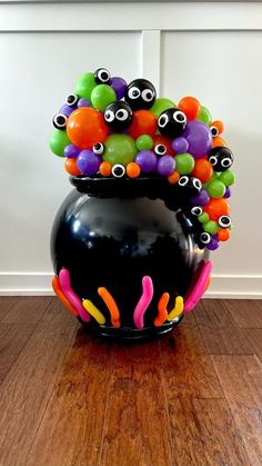 a black vase filled with lots of colorful balls and eyeballs on top of a wooden floor