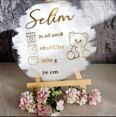 a white sign with gold writing on it and flowers in front of the sign that says selin