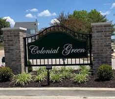 the sign for colonial green is in front of some bushes and trees on either side of the road