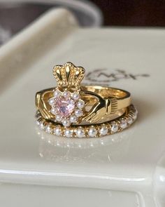 two gold wedding rings with pink and white stones on top of each other in front of a tray