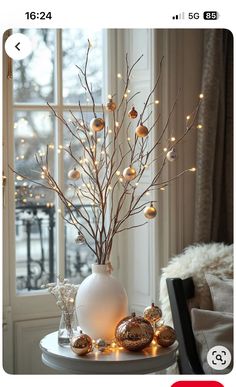 a white vase filled with christmas ornaments on top of a table next to a window