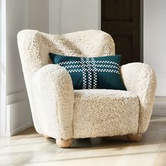 a white chair with a green pillow on it in front of a door and wooden floor