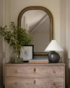 a wooden dresser topped with a lamp and a mirror