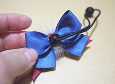 a hand holding a blue and red bow with black bead on it's end