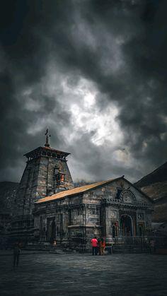 two people standing in front of an old building under a cloudy sky with dark clouds