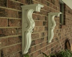 two white decorative brackets on the side of a brick wall next to a planter