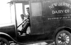 an old black and white photo of two men in the driver's seat of a dairy truck