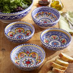 four bowls with different designs on them sitting on a table next to bread and salad