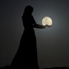 the silhouette of a woman holding her hand out to the moon