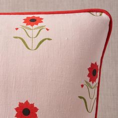 a pink pillow with red flowers and green stems on the front, sitting on a white surface