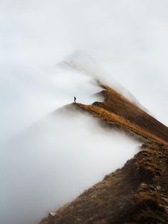 a lone person standing on top of a mountain in the foggy weather with low clouds