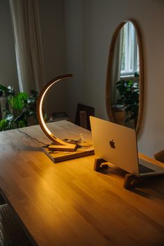 an apple laptop sitting on top of a wooden desk next to a lamp and mirror