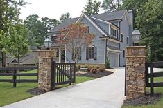 a large house with stone pillars and gated driveway leading to the front yard area