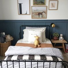 a bed with a black metal frame and white sheets, pillows and stuffed animals on it