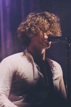 a man with curly hair is singing into a microphone