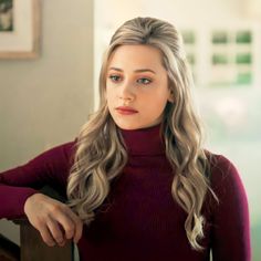 a woman with long blonde hair wearing a turtle neck sweater and looking at the camera