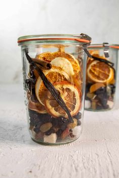 two glass jars filled with orange slices and other food on top of a white table