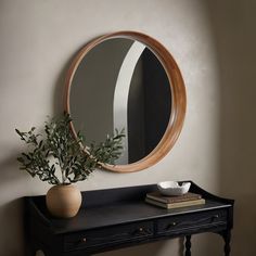 a round mirror on the wall above a table with a vase and book next to it