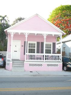 a pink house with white trim on the front porch and balconies is next to a parked car